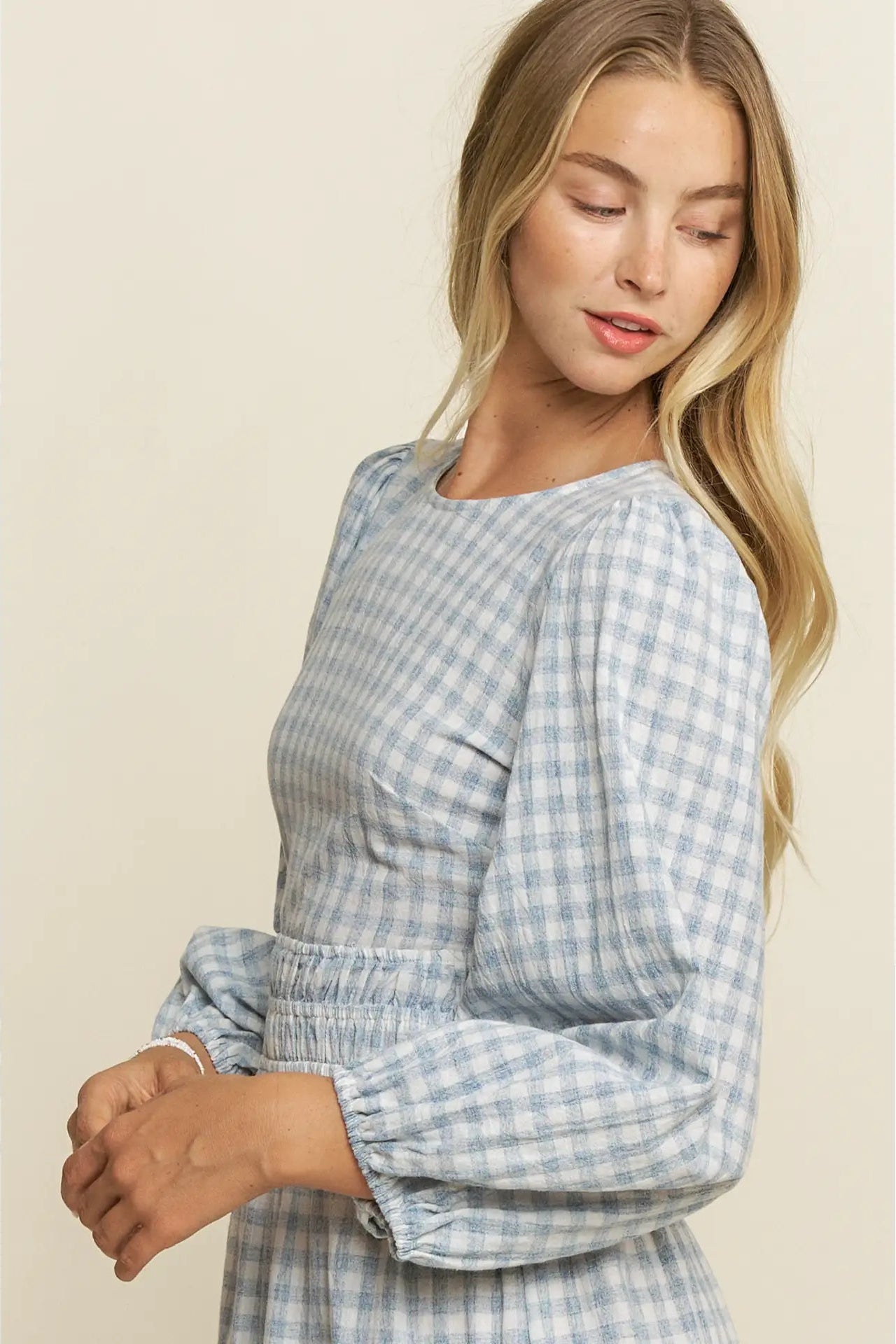 Woman wearing a blue checkered dress against a beige background