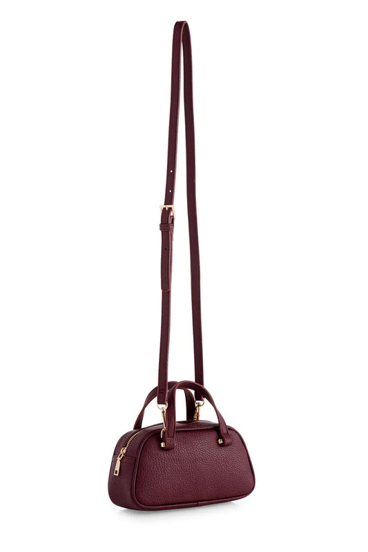 A burgundy pebbled leather crossbody handbag with a long adjustable shoulder strap, dual top handles, and gold-tone hardware, shown against a plain white background.
