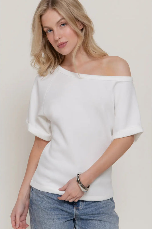 Woman wearing a white off-shoulder top and blue jeans against a plain background