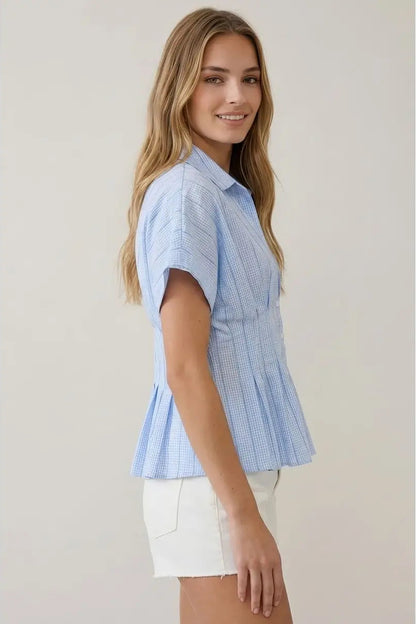 Woman wearing a light blue striped shirt and white shorts on a plain background