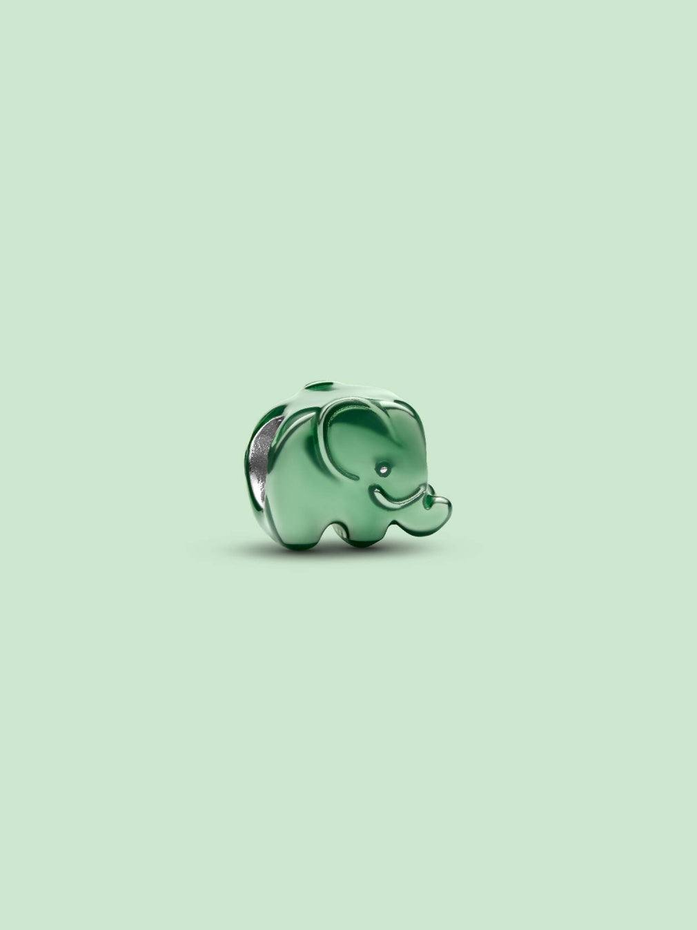 A small glossy green elephant charm or bead with silver-toned edges, centered on a pale mint green background.