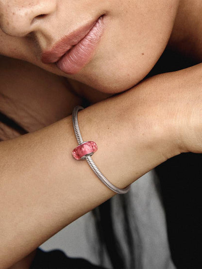Close-up of a wrist wearing a silver bracelet with a pink bead against a blurred background