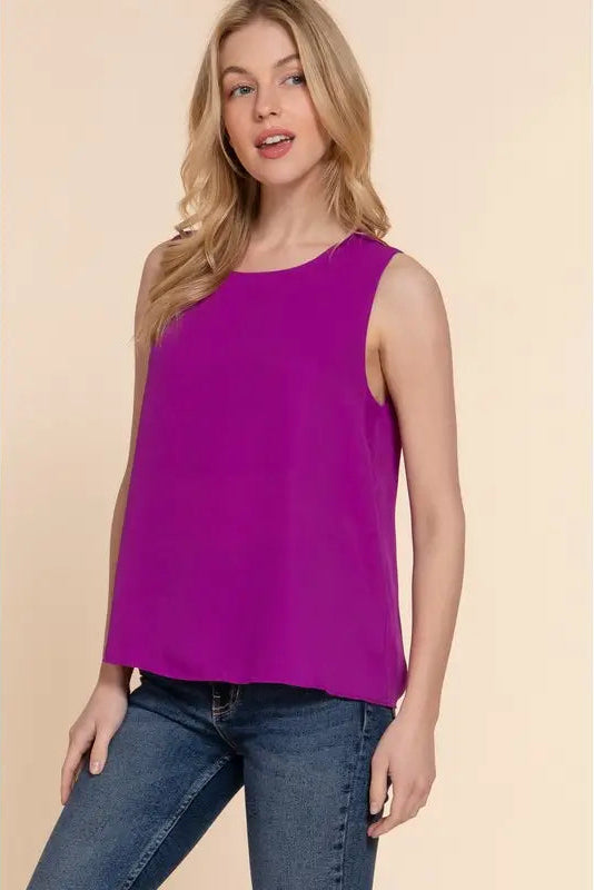 Woman wearing a purple sleeveless top and blue jeans on a beige background