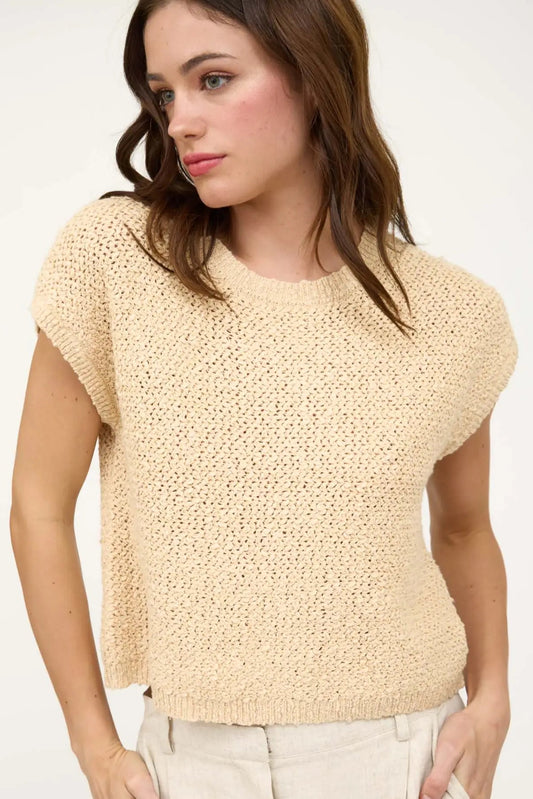 Woman wearing a beige knitted top against a white background