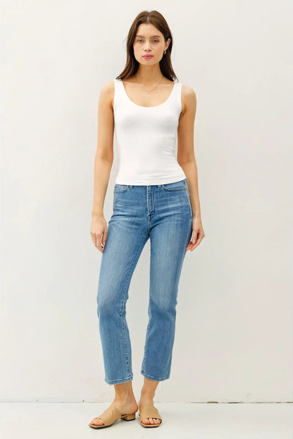 Woman wearing a white tank top and light blue jeans against a plain background