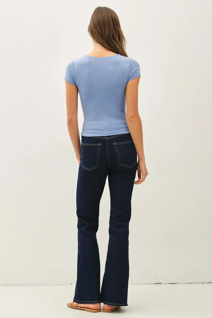 Woman wearing a blue t-shirt and dark jeans against a white background