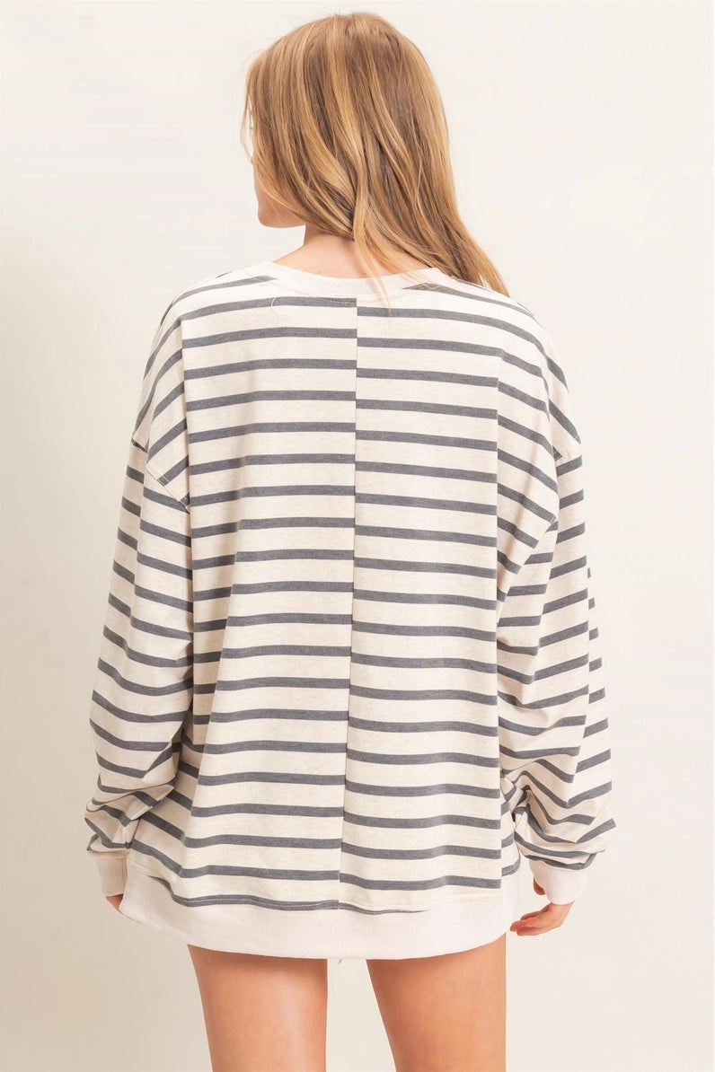 A woman viewed from the back wearing an oversized long-sleeve top with horizontal gray stripes on a cream base, set against a plain light beige studio background.