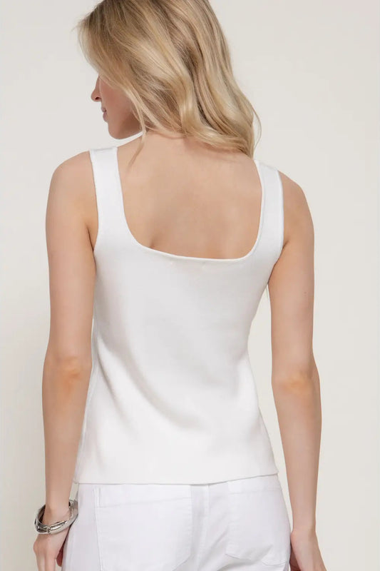 Woman wearing a white tank top against a plain background