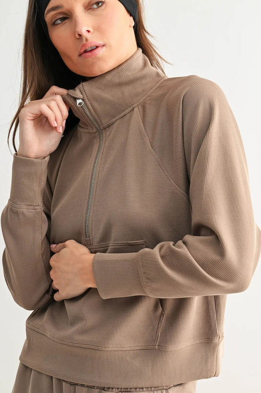 Woman wearing a brown zip-up sweatshirt against a white background