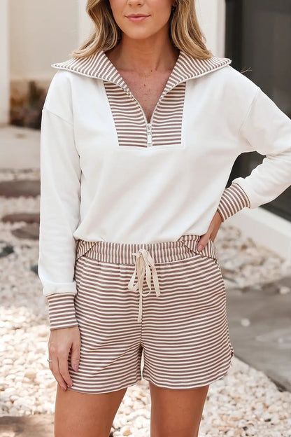 A woman wearing a matching two-piece loungewear set featuring a white long-sleeve quarter-zip top with brown and white striped trim, paired with brown and white striped drawstring shorts.