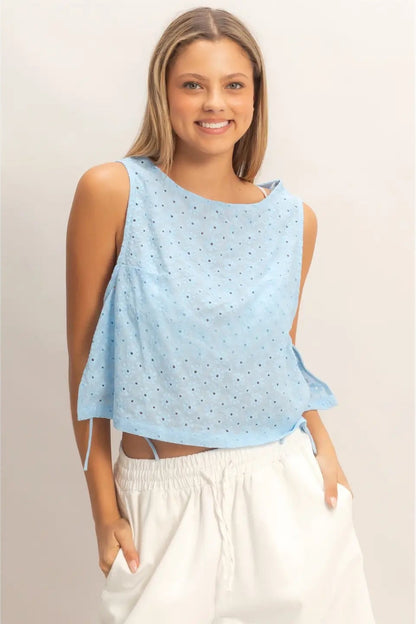 Woman wearing a light blue sleeveless top with white pants on a plain background