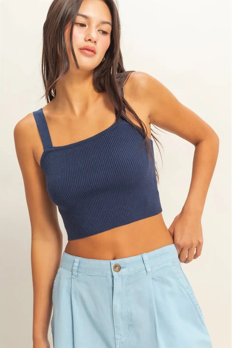 Woman wearing a navy blue one-shoulder top and light blue pants on a plain background