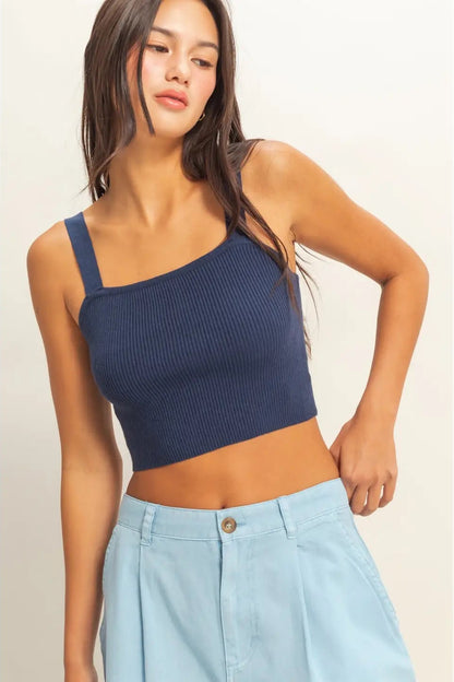 Woman wearing a navy blue one-shoulder top and light blue pants on a plain background
