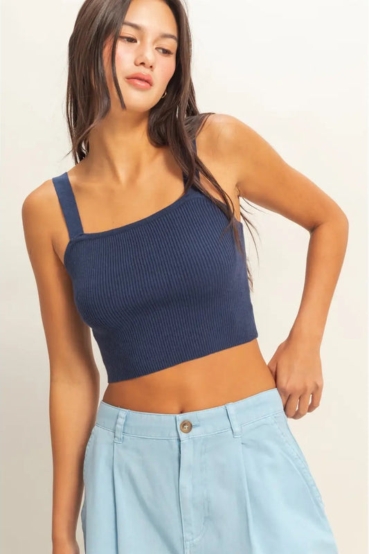 Woman wearing a navy blue one-shoulder top and light blue pants on a plain background