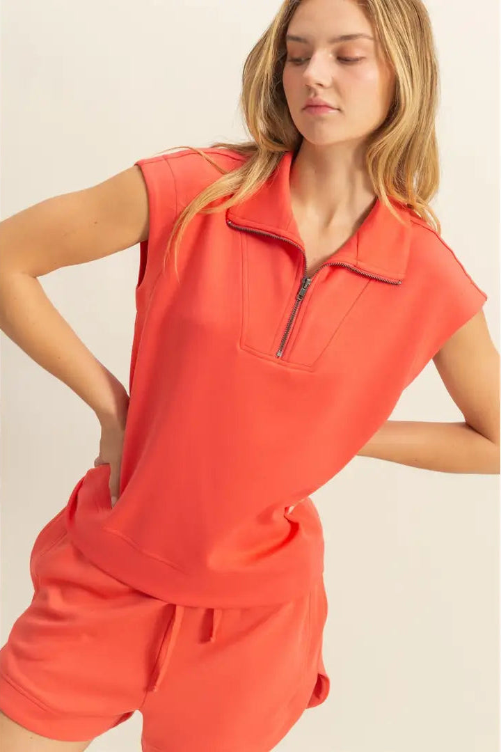 Woman wearing a bright orange sleeveless top and shorts set on a beige background