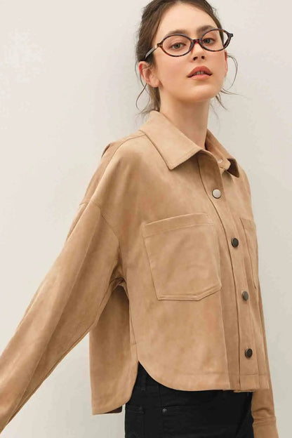 A woman wearing a cropped tan suede-like button-up shirt with a chest pocket, paired with black pants, photographed against a plain light background.