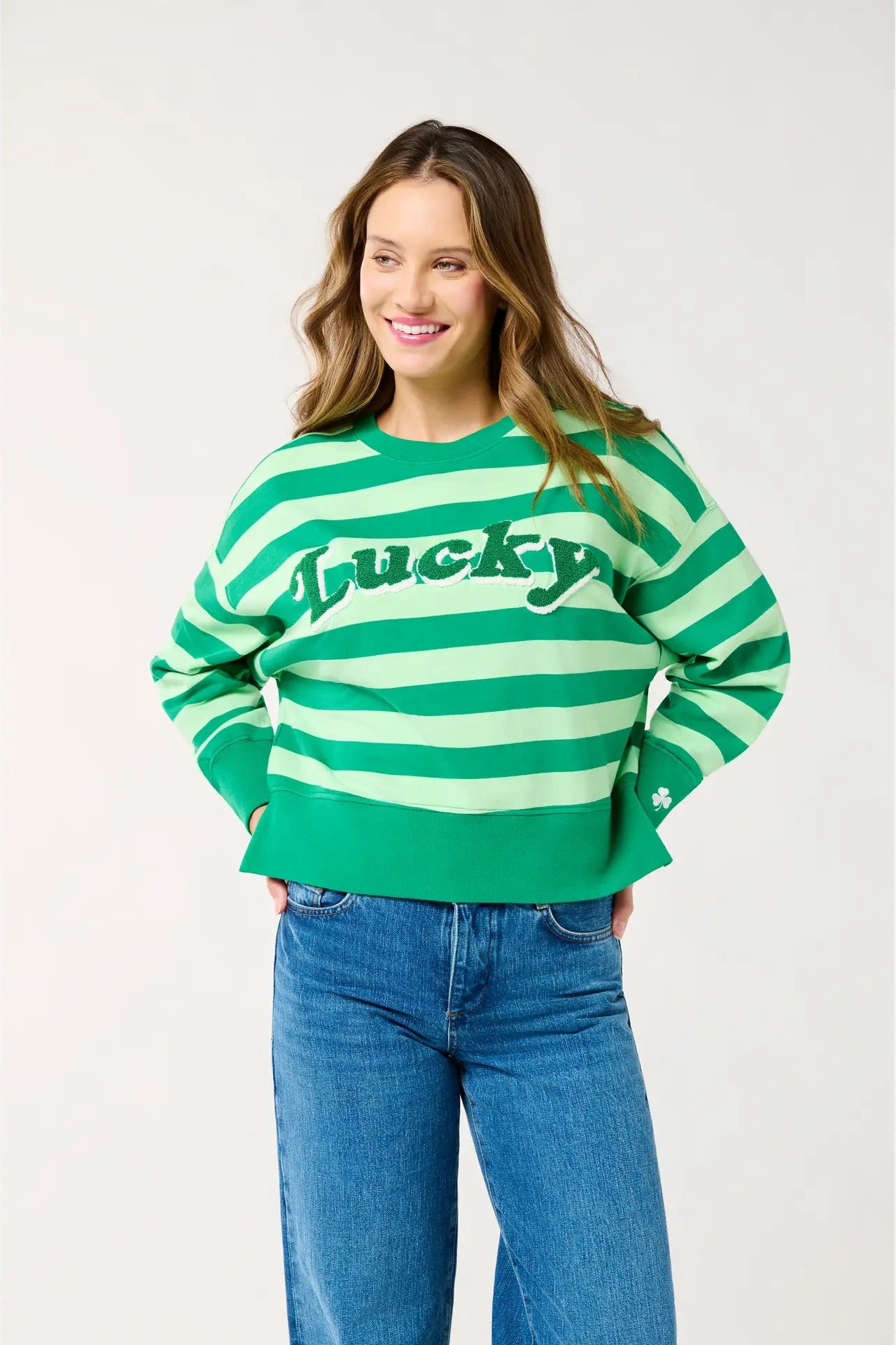 Woman wearing a green and white striped sweater with 'Lucky' text, standing against a plain background.