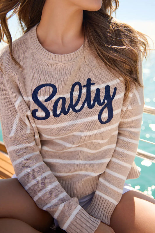 Person wearing a sweater with 'Salty' text by the water