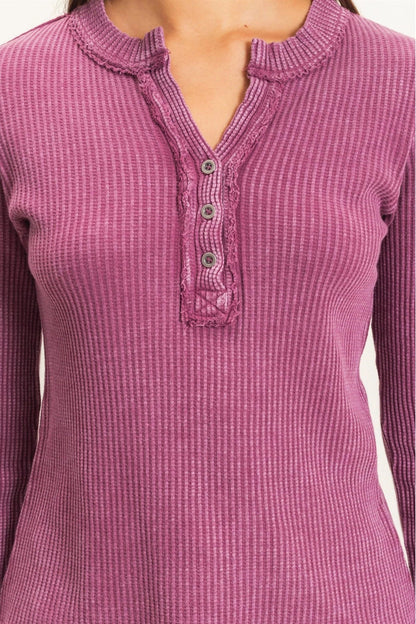 A close-up of a woman wearing a ribbed long-sleeve henley top in a dusty rose or mauve pink color, featuring a buttoned split neckline.