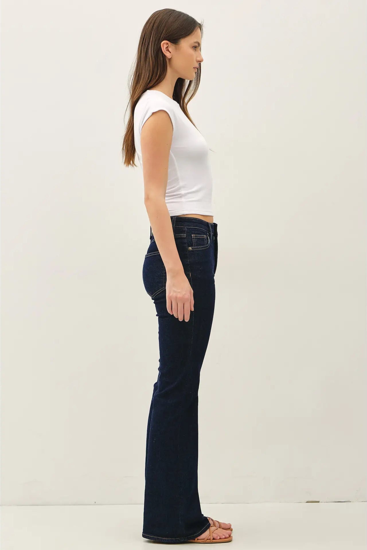 Woman wearing dark blue jeans and a white top on a light background