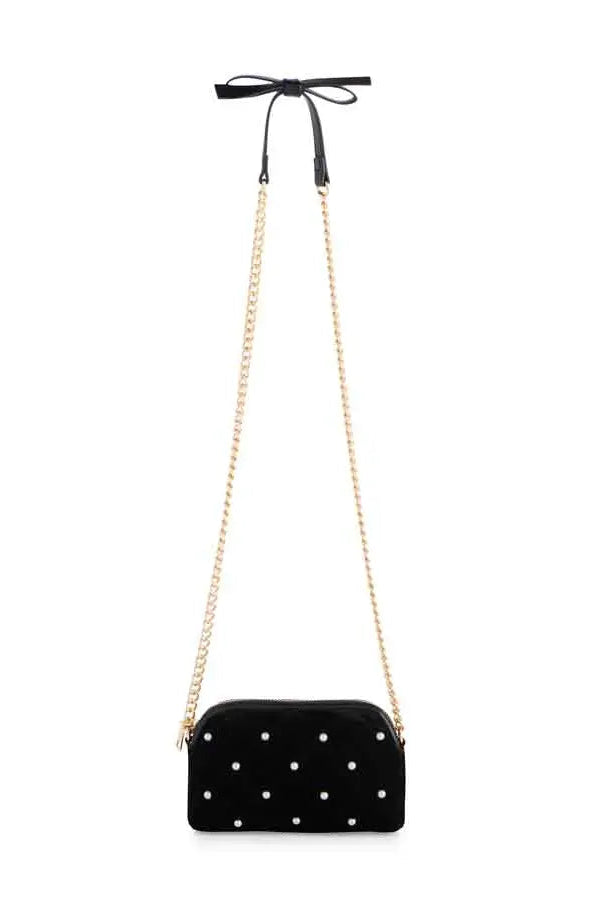 A black velvet crossbody bag with white polka dots, featuring a gold-tone chain strap and a black ribbon bow at the top, shown against a plain white background.