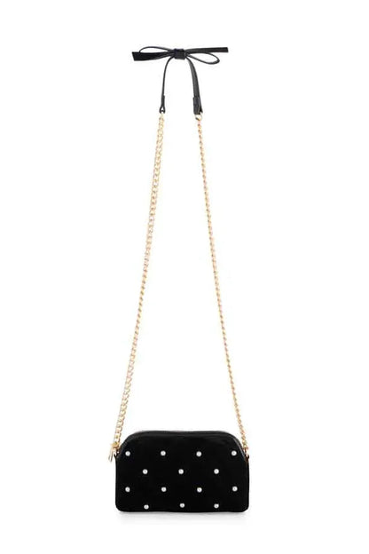 A black velvet crossbody bag with white polka dots, featuring a gold-tone chain strap and a black ribbon bow at the top, shown against a plain white background.