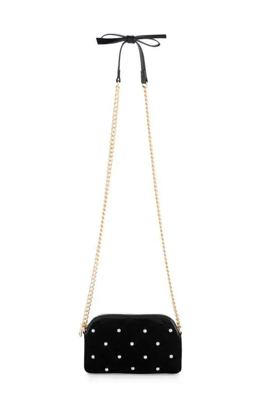A black velvet crossbody bag with white polka dots, featuring a gold-tone chain strap and a black ribbon bow at the top, shown against a plain white background.