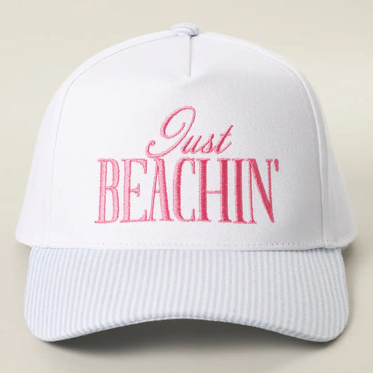 White cap with pink 'Just BEACHIN'' text on a beige background