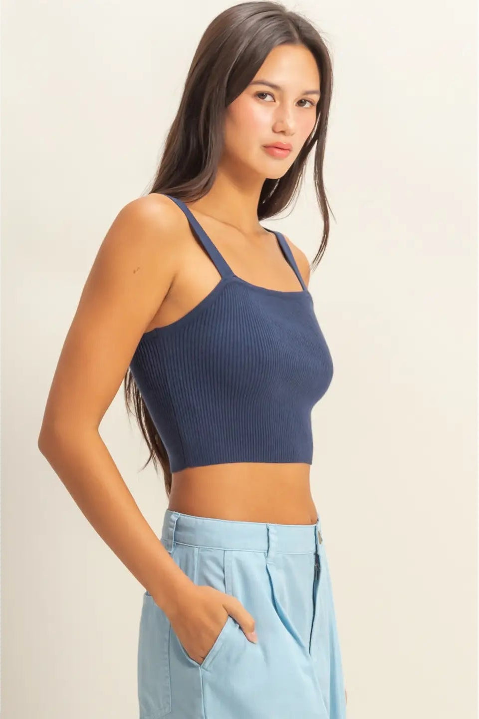 Woman wearing a blue ribbed crop top and light blue pants on a beige background