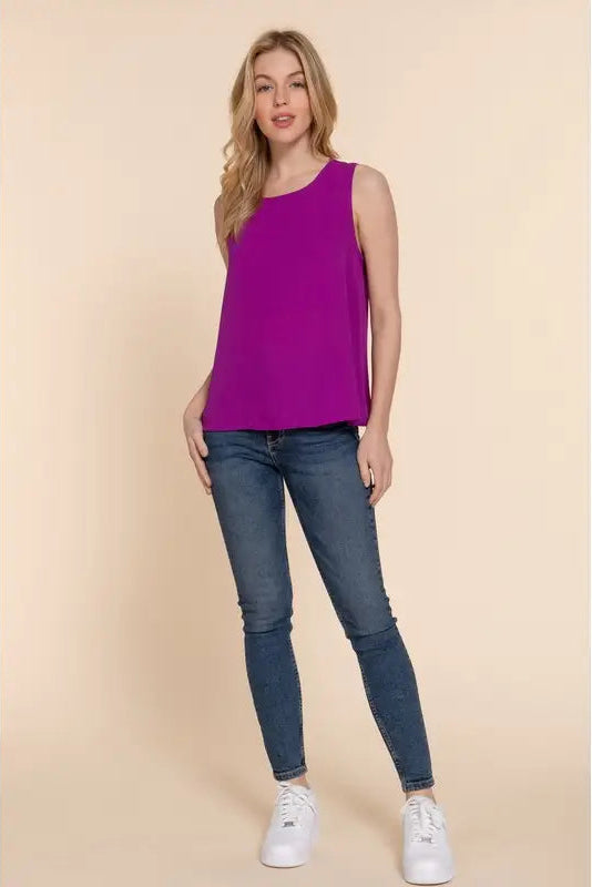 Woman wearing a purple sleeveless top and blue jeans on a beige background