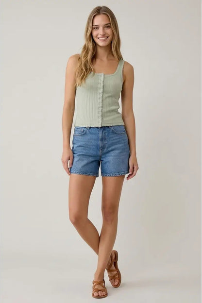 Woman wearing a light green tank top and blue denim shorts on a plain background