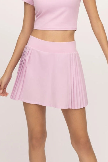Woman wearing a pink outfit with a pleated skirt on a white background