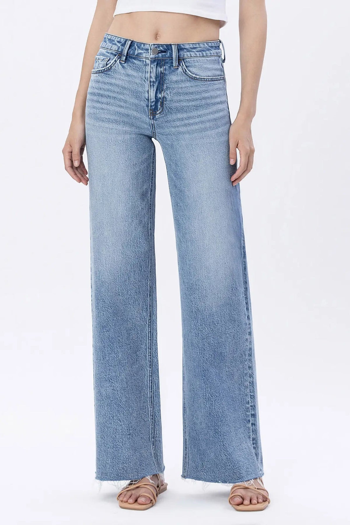 A model wearing light blue wide-leg denim jeans with a faded wash, paired with a white crop top and flat sandals, shown against a plain white studio background.