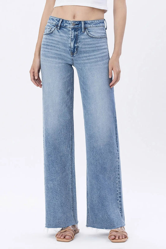 A model wearing light blue wide-leg denim jeans with a faded wash, paired with a white crop top and flat sandals, shown against a plain white studio background.