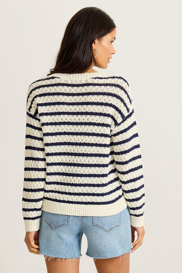 Woman wearing a striped sweater and denim shorts on a plain background