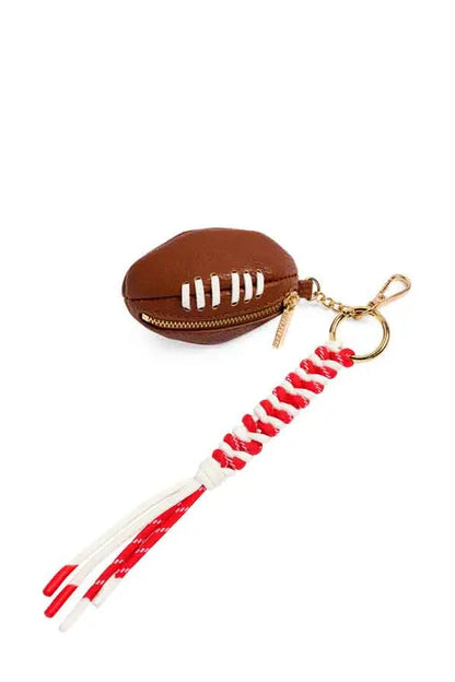 A football-shaped zippered pouch keychain in brown faux leather with white laces, attached to a red and white braided cord tassel with gold-tone hardware, shown on a plain white background.