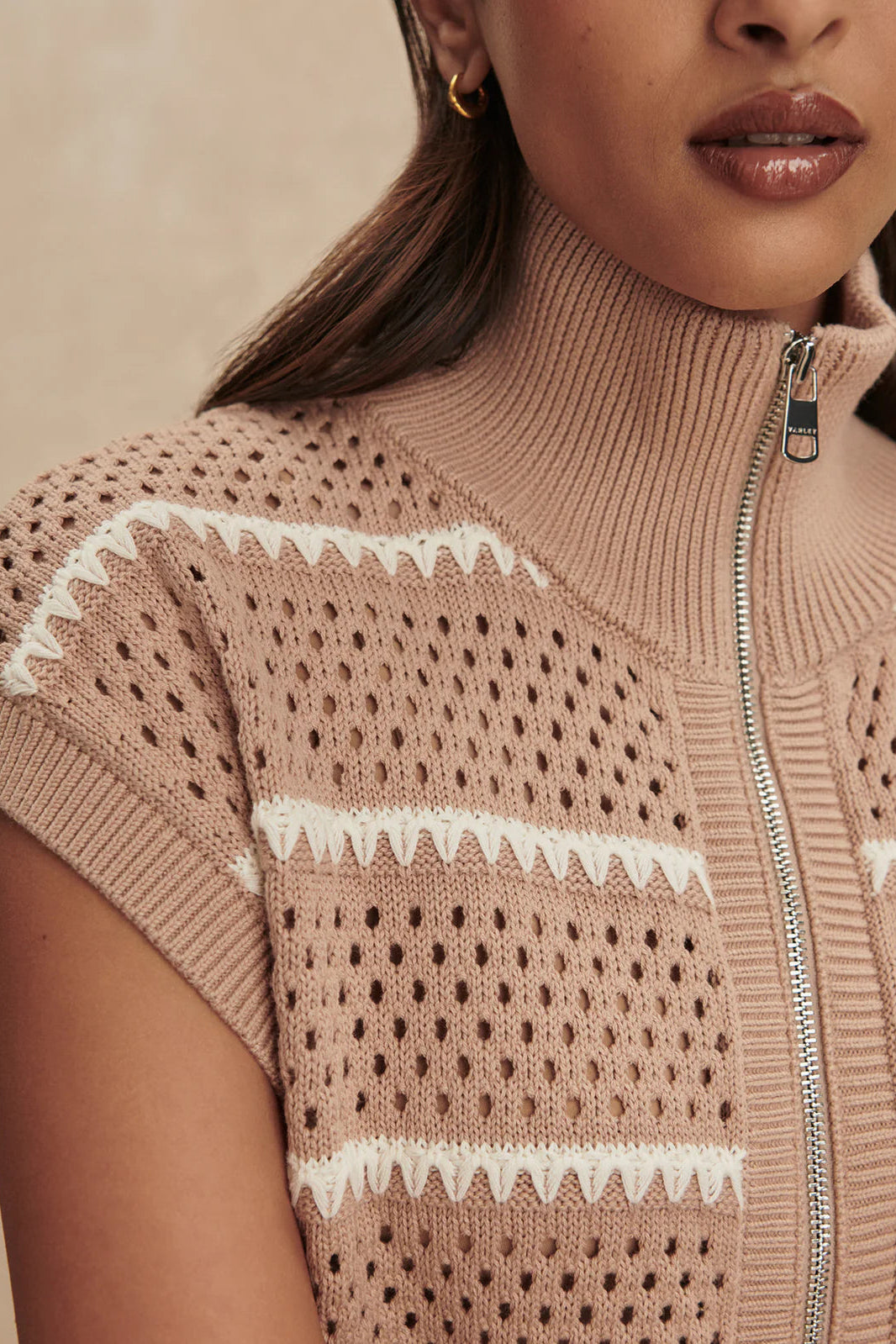 Close-up of a person wearing a patterned beige sweater with a zipper.