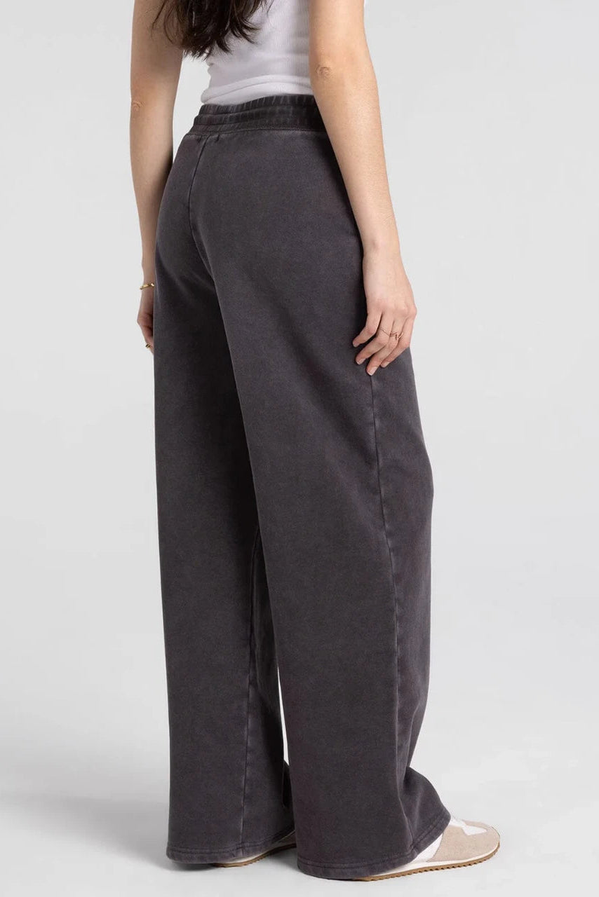 A model shown from the back wearing dark gray wide-leg jeans, a white tank top, and beige flat shoes against a light gray studio background.