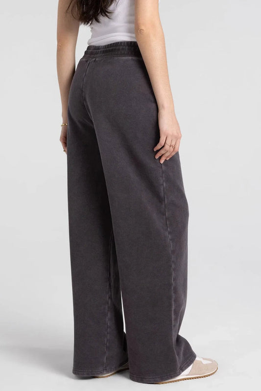 A model shown from the back wearing dark gray wide-leg jeans, a white tank top, and beige flat shoes against a light gray studio background.