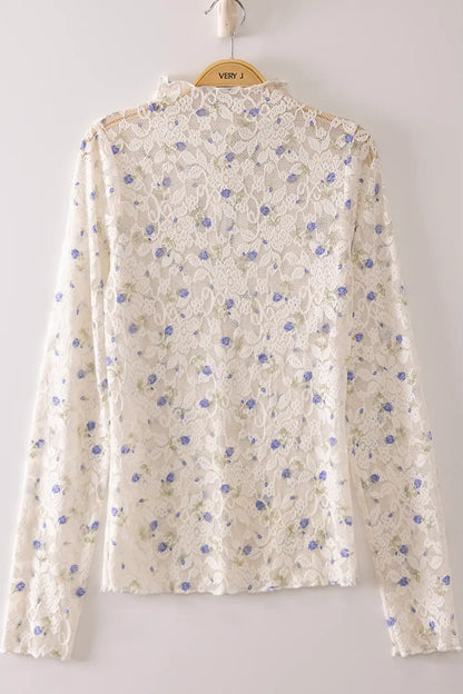 An off-white lace long-sleeve blouse with a blue floral pattern, hanging on a wooden hanger against a light gray background.