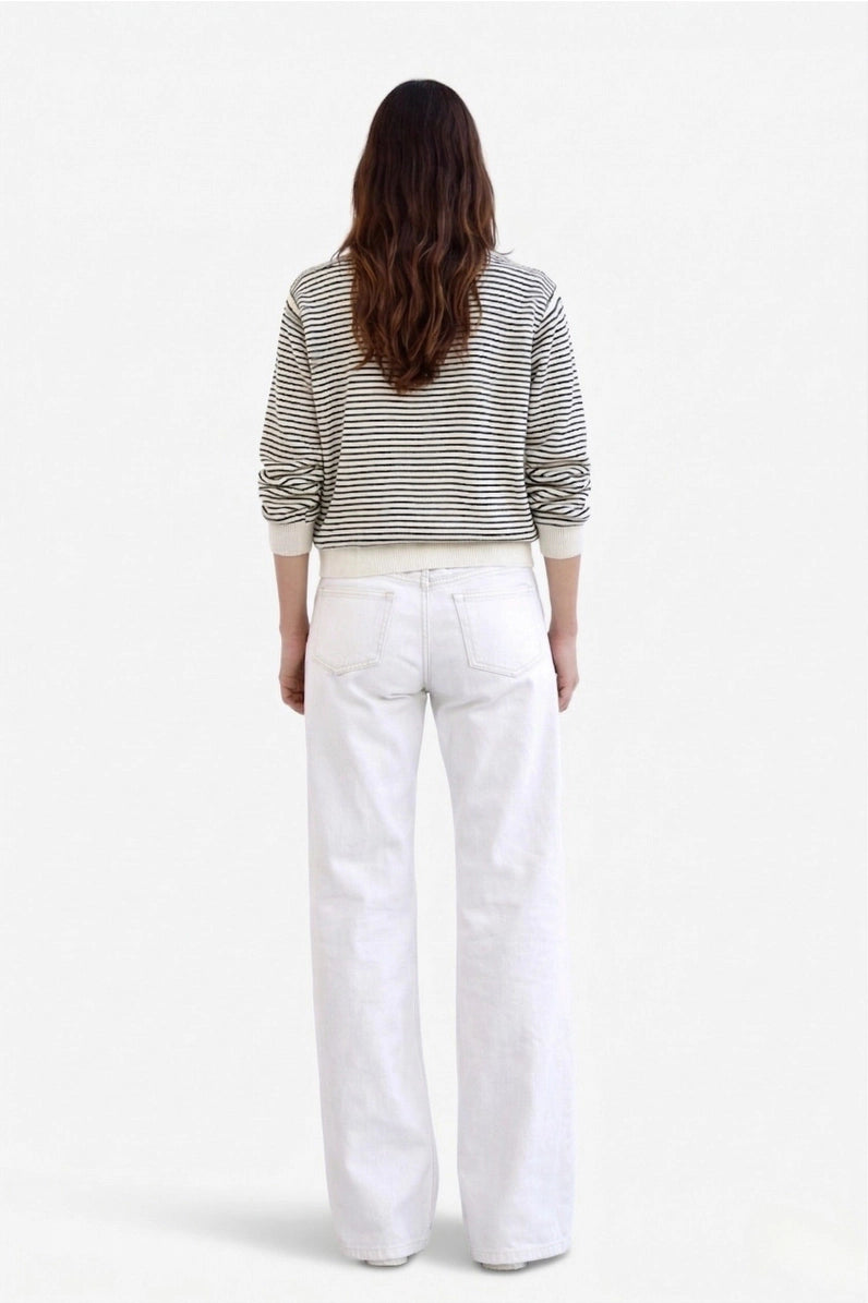 A woman viewed from behind wearing a black and white horizontally striped long-sleeve top and white wide-leg jeans, set against a plain white studio background.