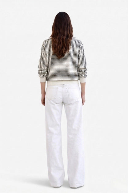 A woman viewed from behind wearing a black and white horizontally striped long-sleeve top and white wide-leg jeans, set against a plain white studio background.