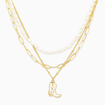 Layered gold and pearl necklaces with a cowboy boot charm on a white background