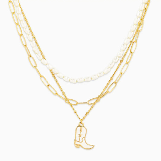 Layered gold and pearl necklaces with a cowboy boot charm on a white background