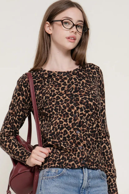 A woman wearing a brown and black leopard print long-sleeve knit top, paired with blue jeans and a burgundy shoulder bag, against a plain off-white background.