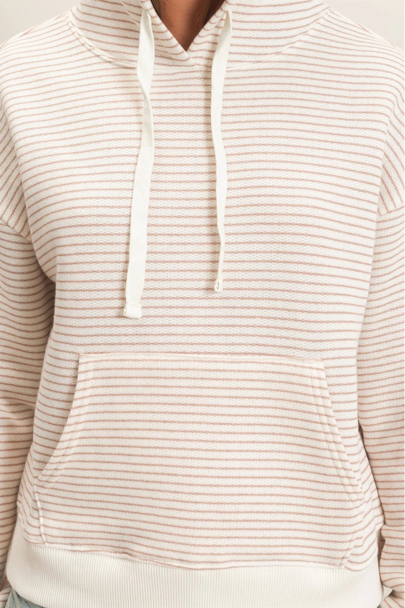 A close-up of a person wearing a cream-colored hoodie with thin, evenly spaced light brown horizontal stripes. The hoodie features a front kangaroo pocket and matching drawstrings.