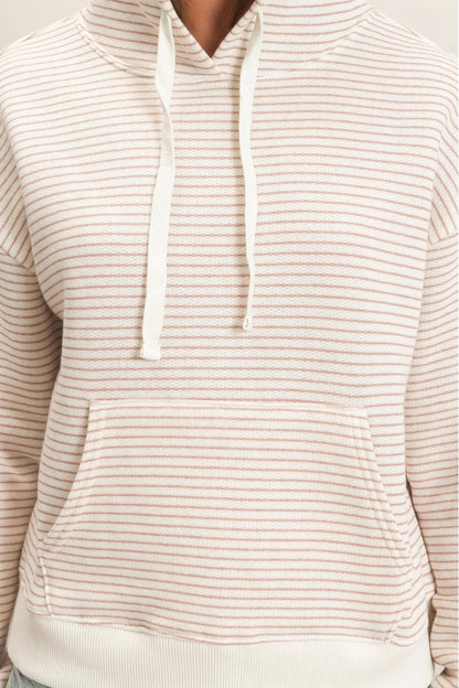 A close-up of a person wearing a cream-colored hoodie with thin, evenly spaced light brown horizontal stripes. The hoodie features a front kangaroo pocket and matching drawstrings.
