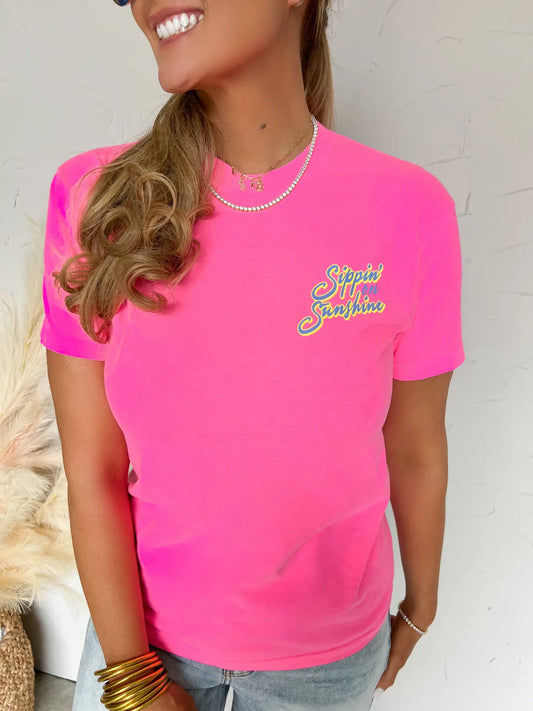 Woman wearing a bright pink t-shirt with text, standing against a neutral background.