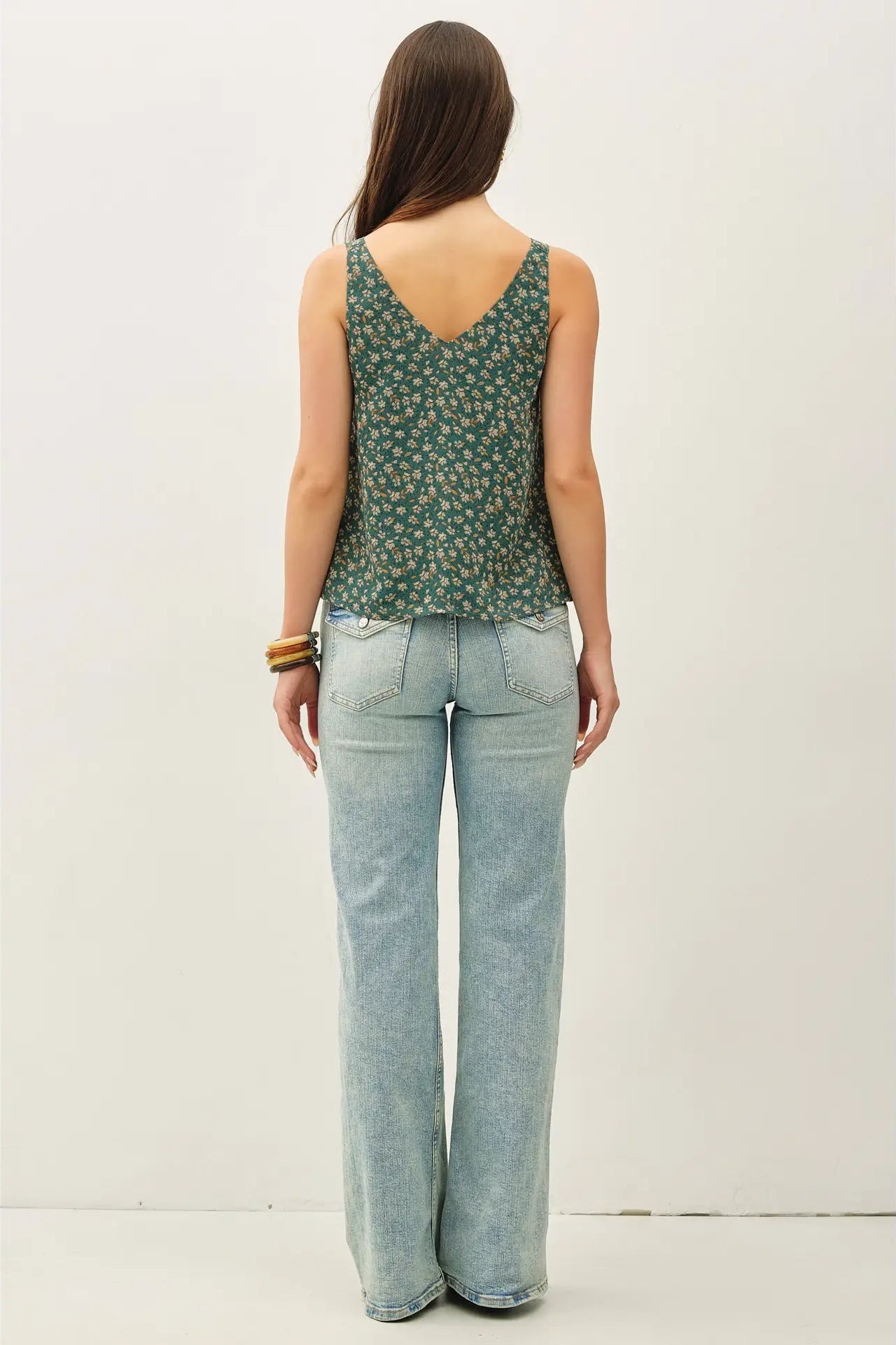 Woman wearing a green floral tank top and light blue jeans against a white background