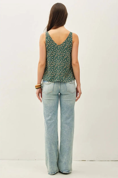 Woman wearing a green floral tank top and light blue jeans against a white background